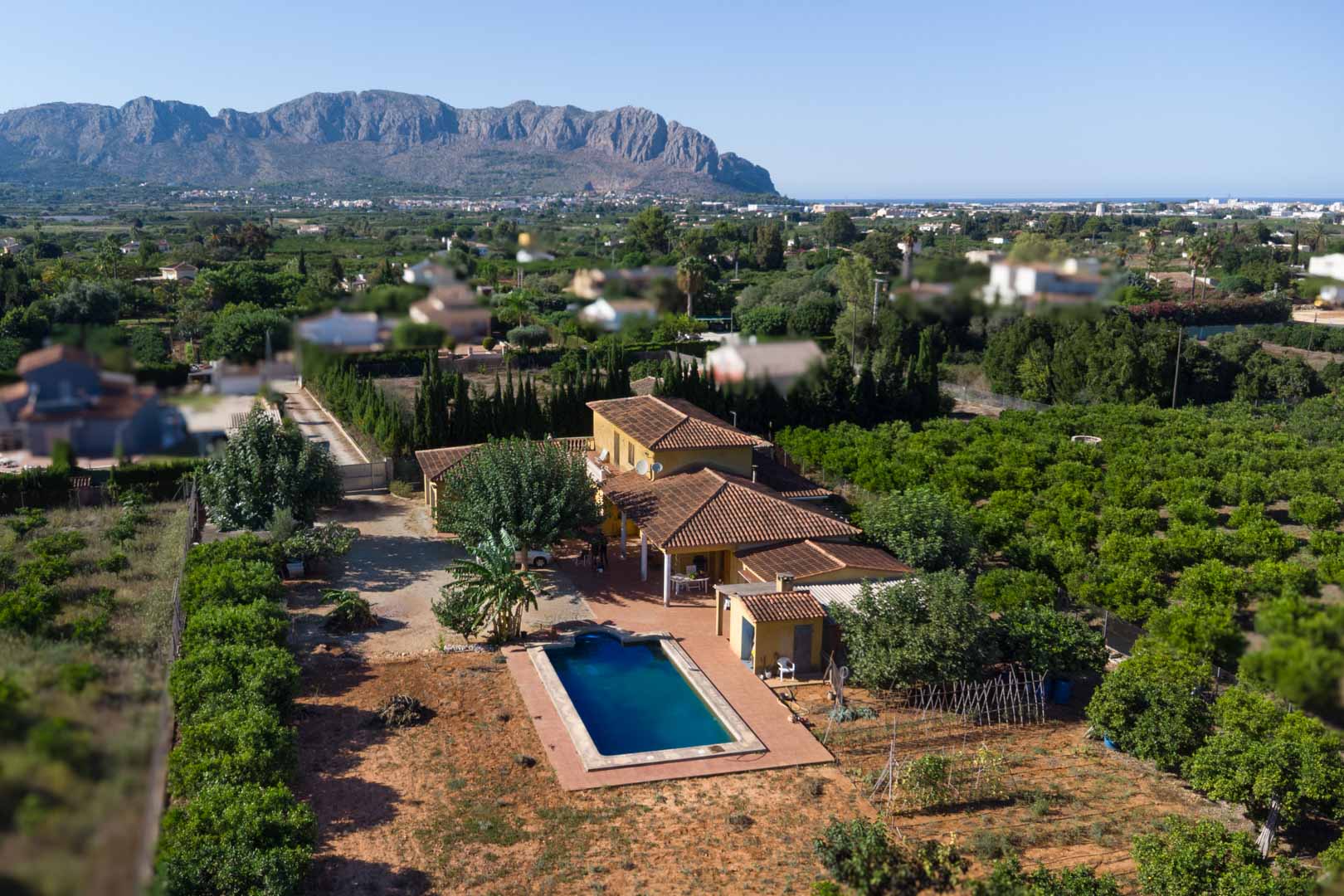Vue aérienne de la villa avec toiture en terre cuite, piscine privée et vastes vergers d'agrumes face à l'imposante montagne de Segaria.