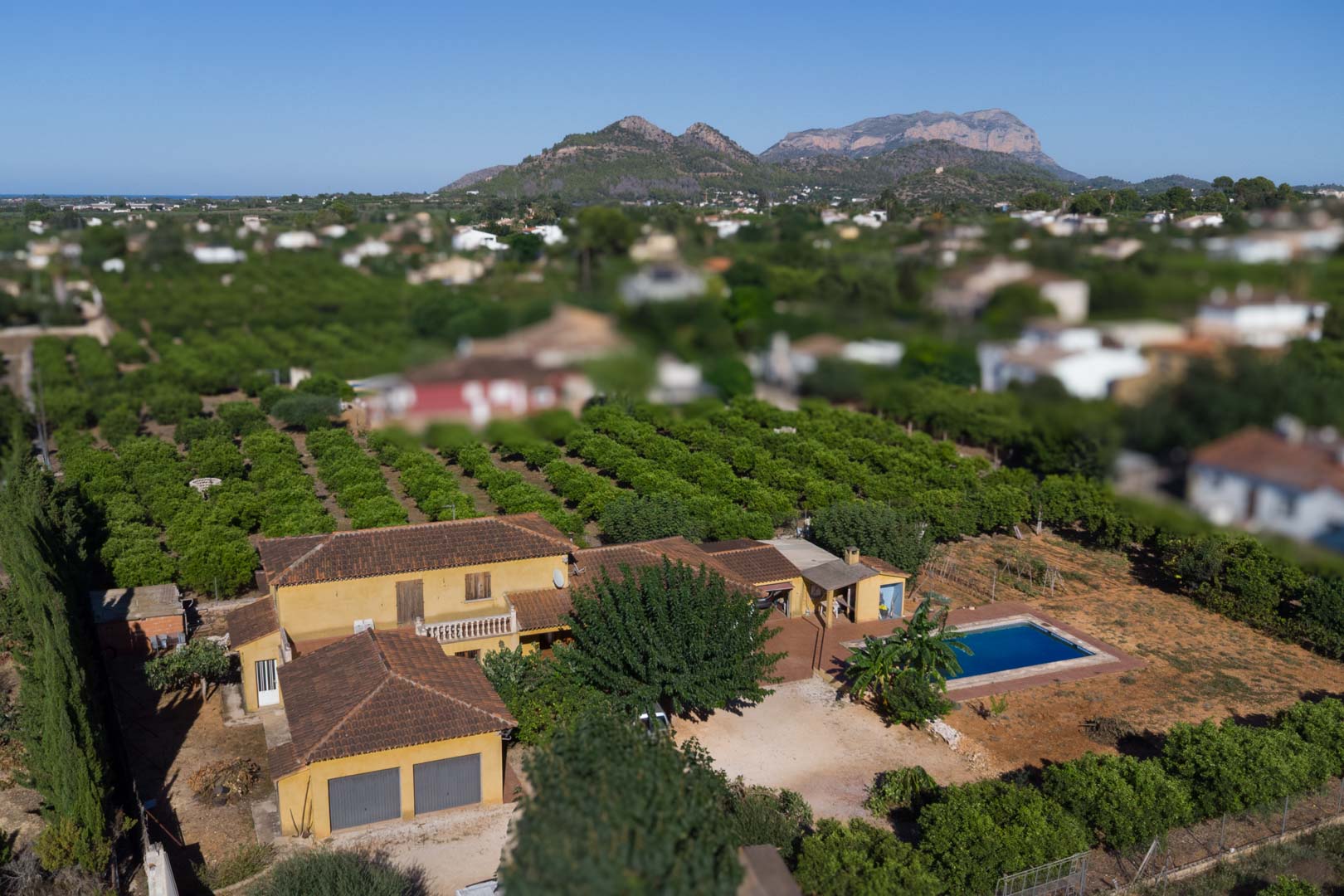 Vue aérienne de la villa rustique avec sa piscine privée, ses vastes vergers d'agrumes et une vue imprenable sur la montagne Segaria en arrière-plan.