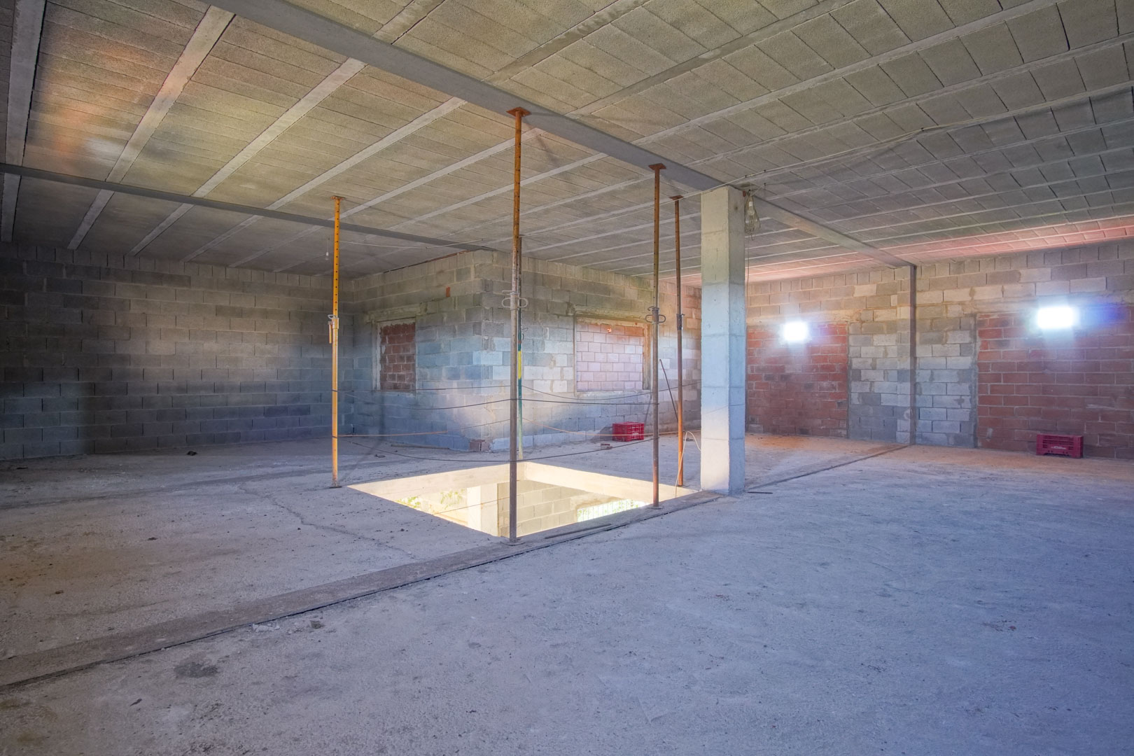 Étage supérieur spacieux en cours de rénovation avec murs en parpaings, piliers en béton et ouverture centrale prévue pour l'escalier.