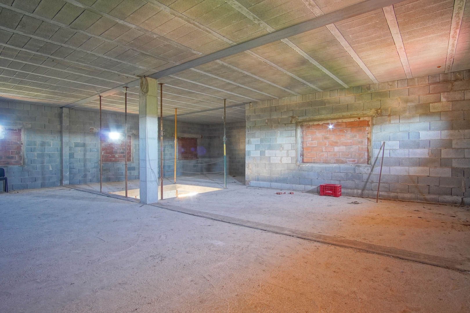 Intérieur à aire ouverte en état de gros œuvre avec murs en blocs de béton, poutres en acier et trémie d'escalier, prêt pour un aménagement personnalisé.