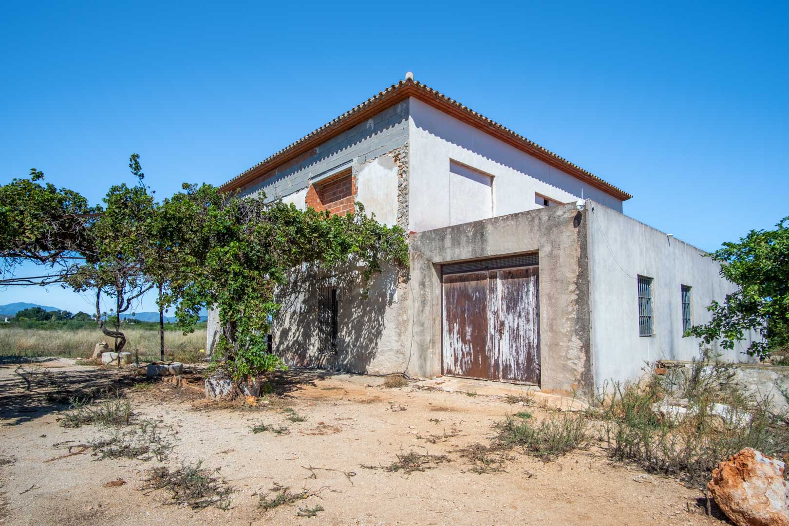 Vue extérieure de la maison de campagne en cours de rénovation, avec sa structure consolidée, son terrain plat et une vue dégagée sur les montagnes.