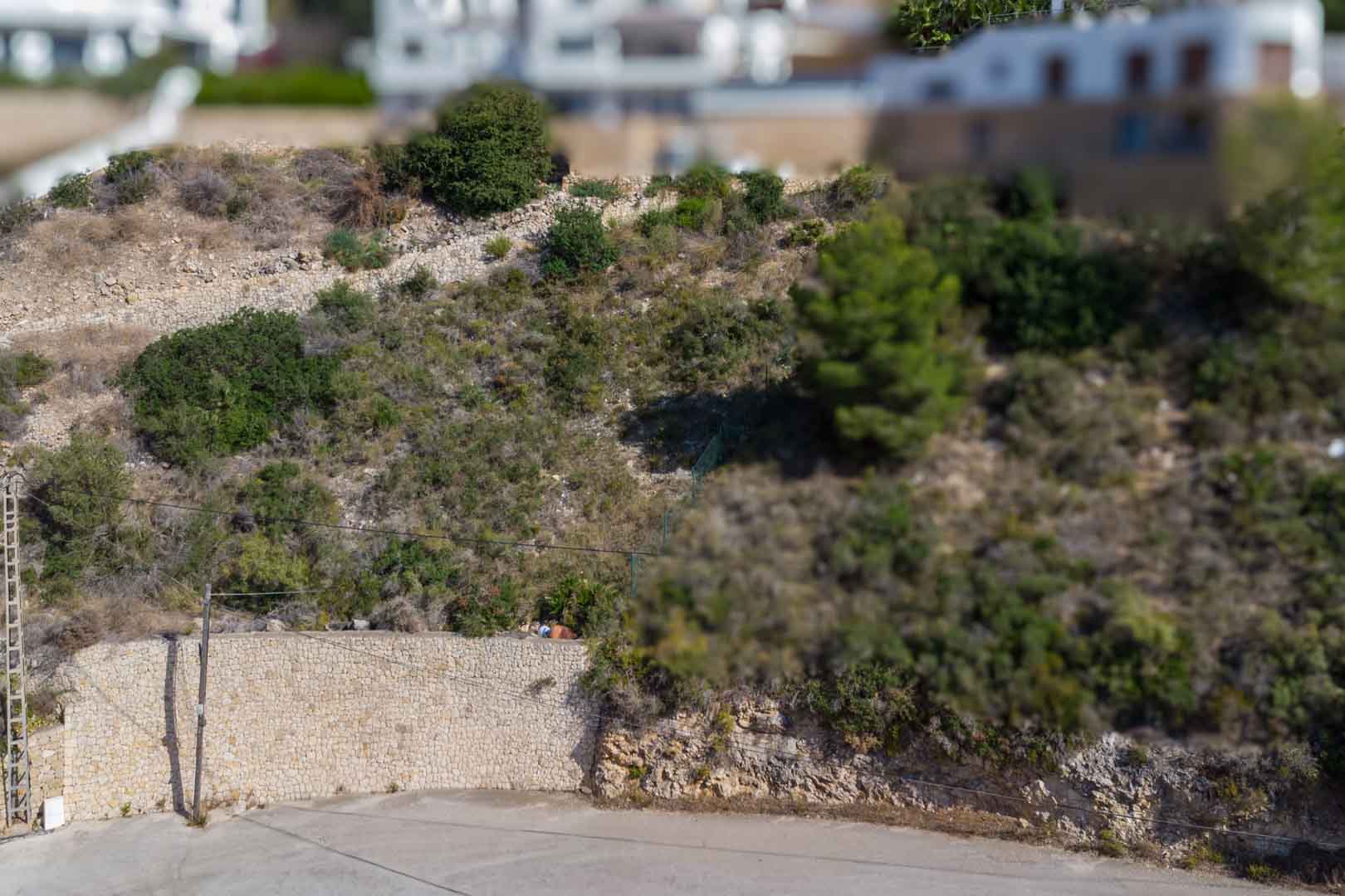 Terrain urbain en pente avec murs de soutènement en pierre naturelle et végétation locale, situé dans un quartier résidentiel calme.