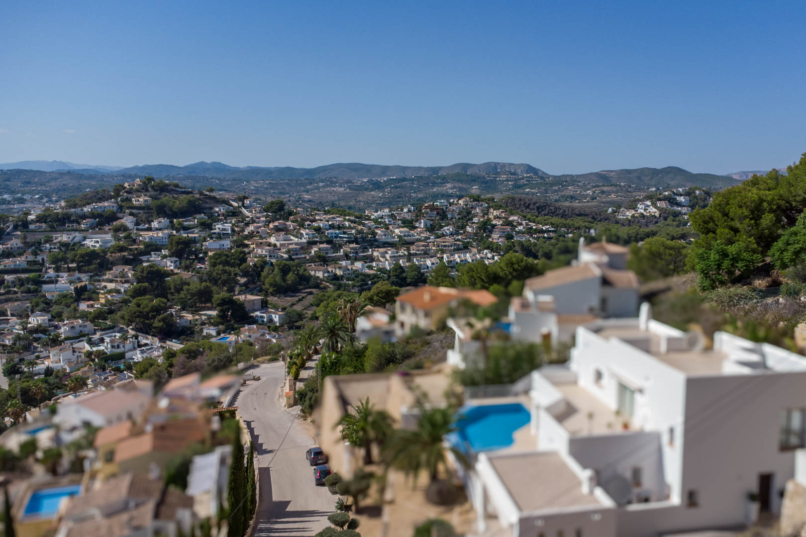 Vue panoramique surélevée du quartier d'El Portet, révélant des villas blanches avec piscines privées et un paysage vallonné sous un ciel azur.