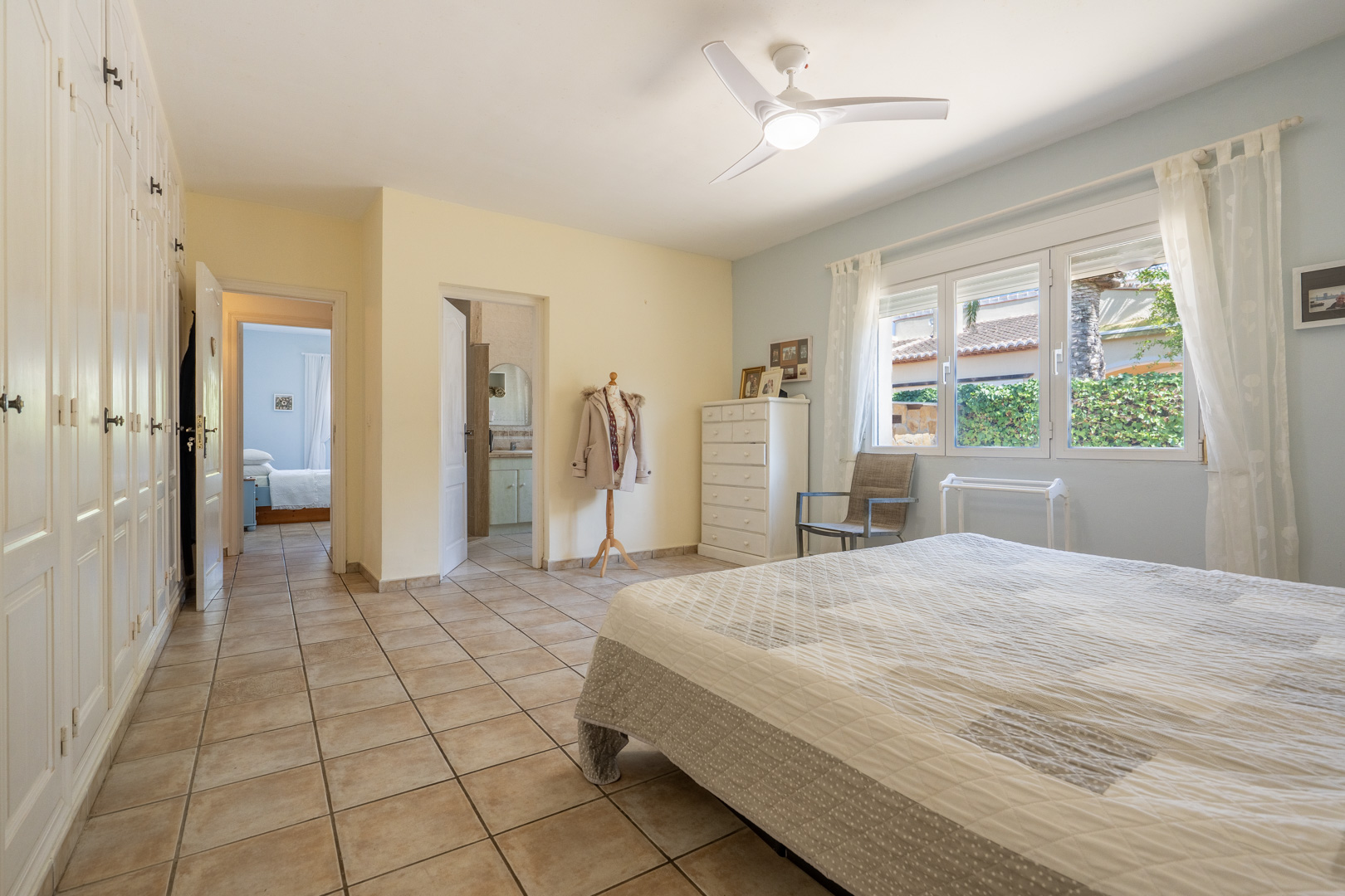 Chambre lumineuse avec placards intégrés, ventilateur de plafond et salle de bain attenante. Carrelage crème.