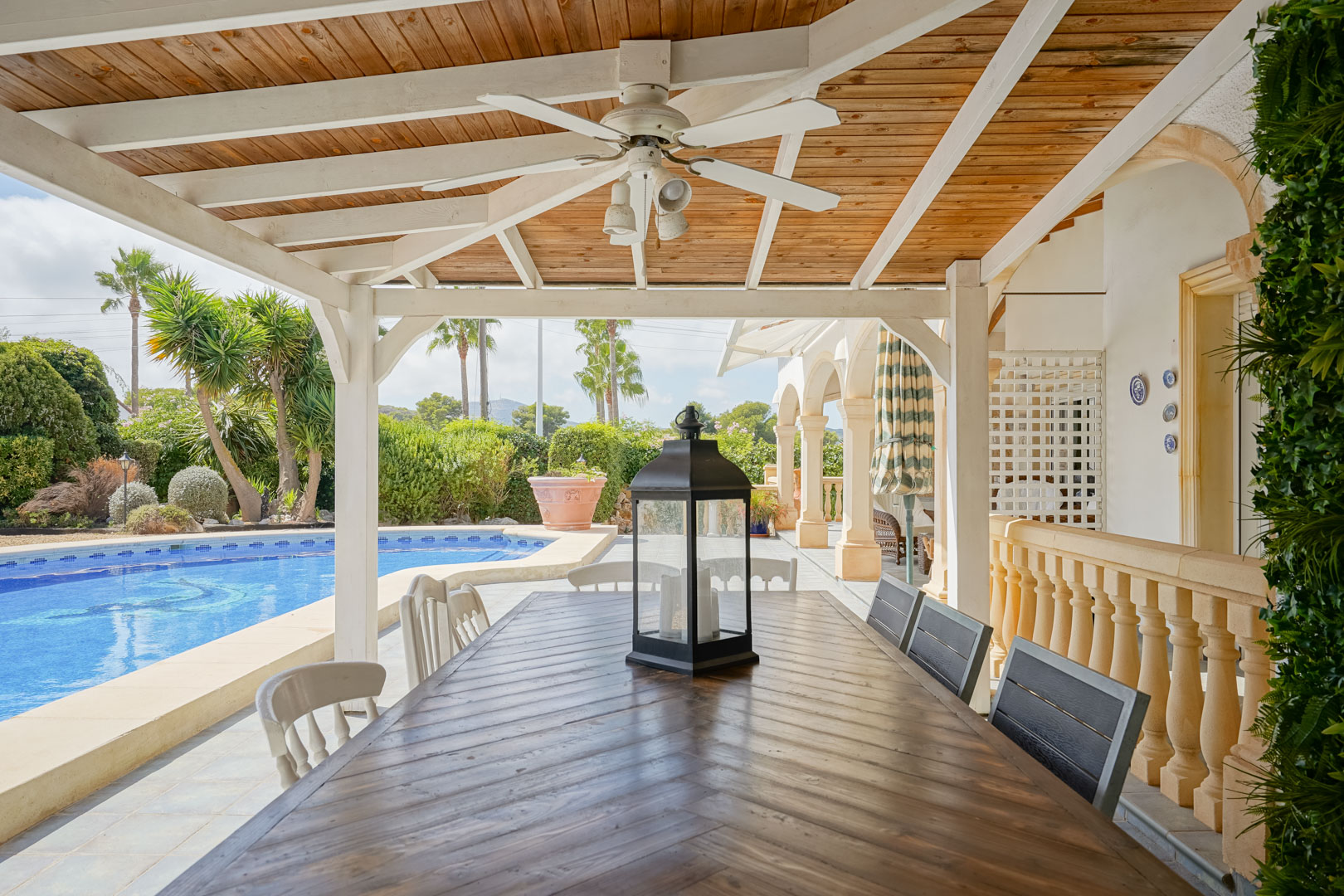Terrasse couverte avec table en bois, vue sur la piscine et le jardin à Jávea.