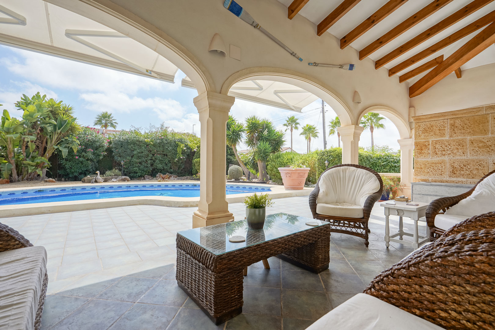 Terrasse couverte avec vue sur la piscine. Mobilier en rotin et table basse en verre.