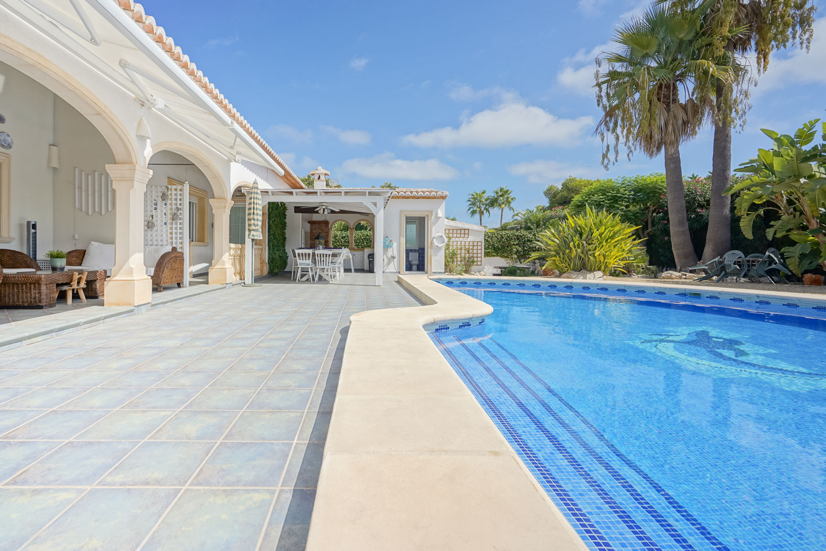 Vue sur la piscine avec des carreaux bleus et terrasse avec des colonnes en pierre à Jávea.