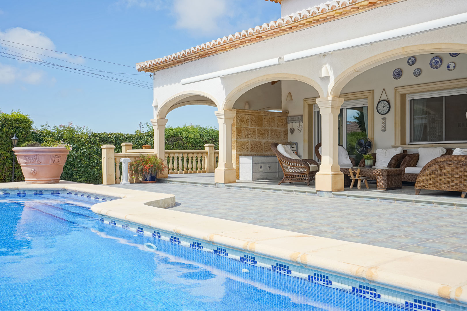 Vue sur la piscine et terrasse couverte avec arches et mobilier en osier à Jávea.