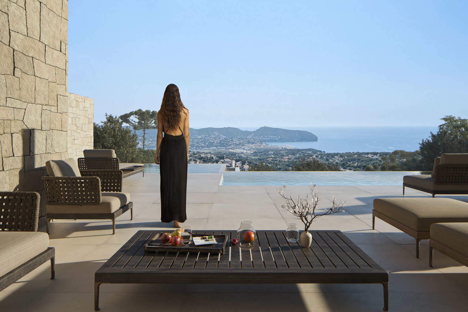 Terrasse extérieure avec mobilier design, mur en pierre naturelle et piscine à débordement offrant une vue panoramique sur la mer Méditerranée et Moraira.