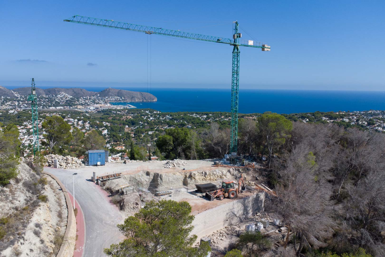 Vue aérienne du terrain en phase de terrassement avec grue de chantier, offrant un panorama dégagé sur la mer Méditerranée et la côte de Moraira.