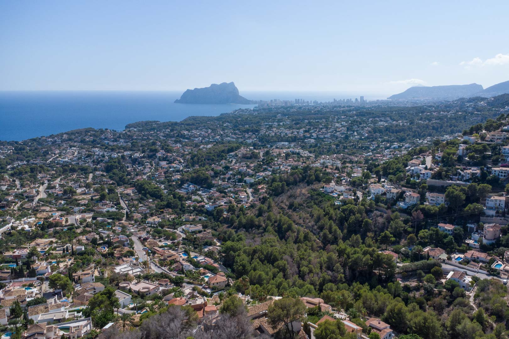 Vue aérienne panoramique de la côte de Moraira et Calpe, avec le Peñón de Ifach s'élevant au-dessus de la Méditerranée et des collines verdoyantes.