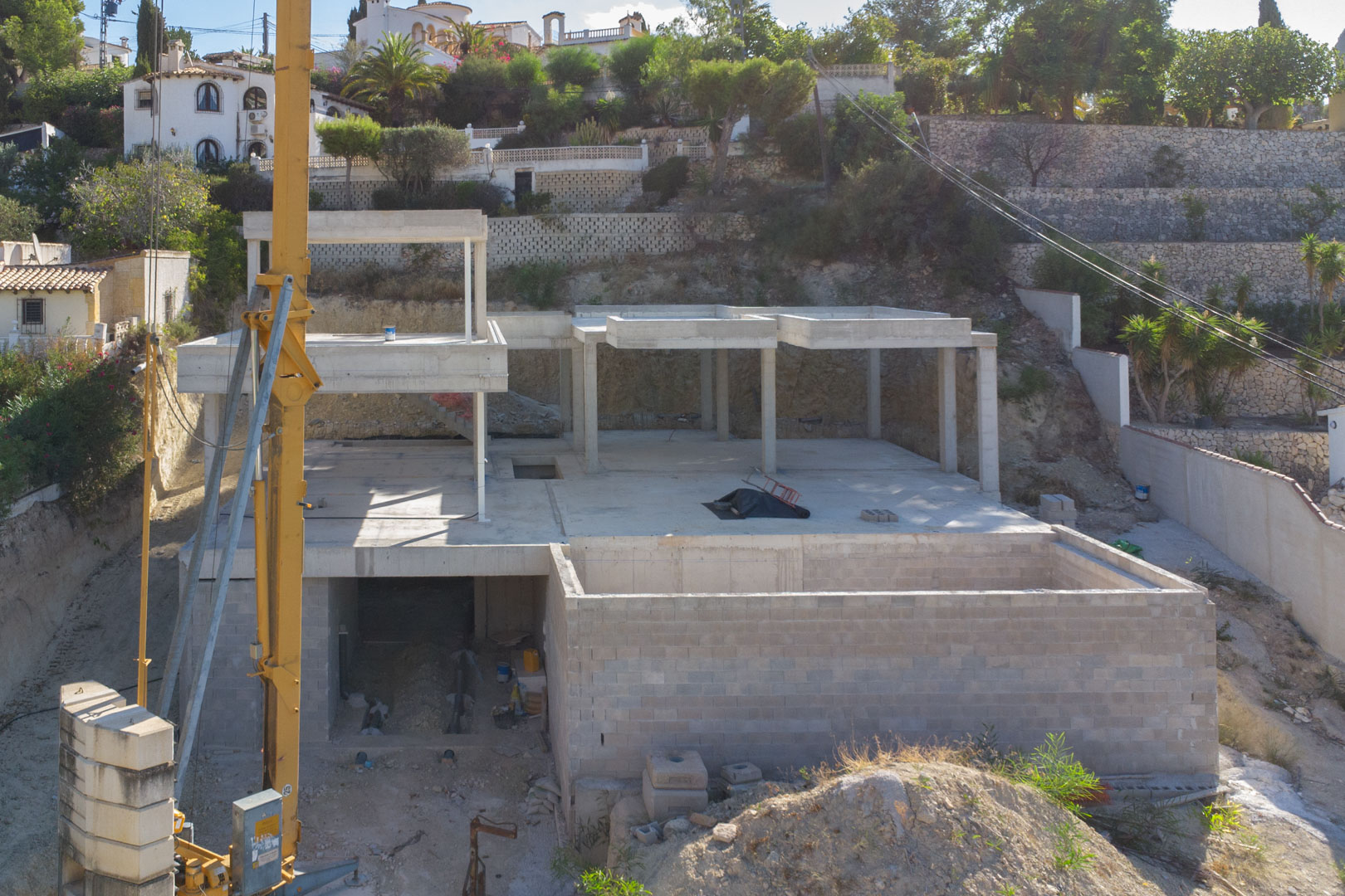Vue de la structure en béton armé en cours de construction, illustrant les différents niveaux de la villa et les murs de soutènement en pierre.