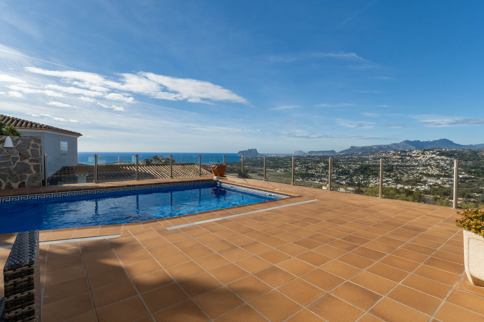 Terrasse en terre cuite avec piscine privée et garde-corps en verre, offrant une vue panoramique sur la mer Méditerranée et le célèbre Peñón de Ifach.