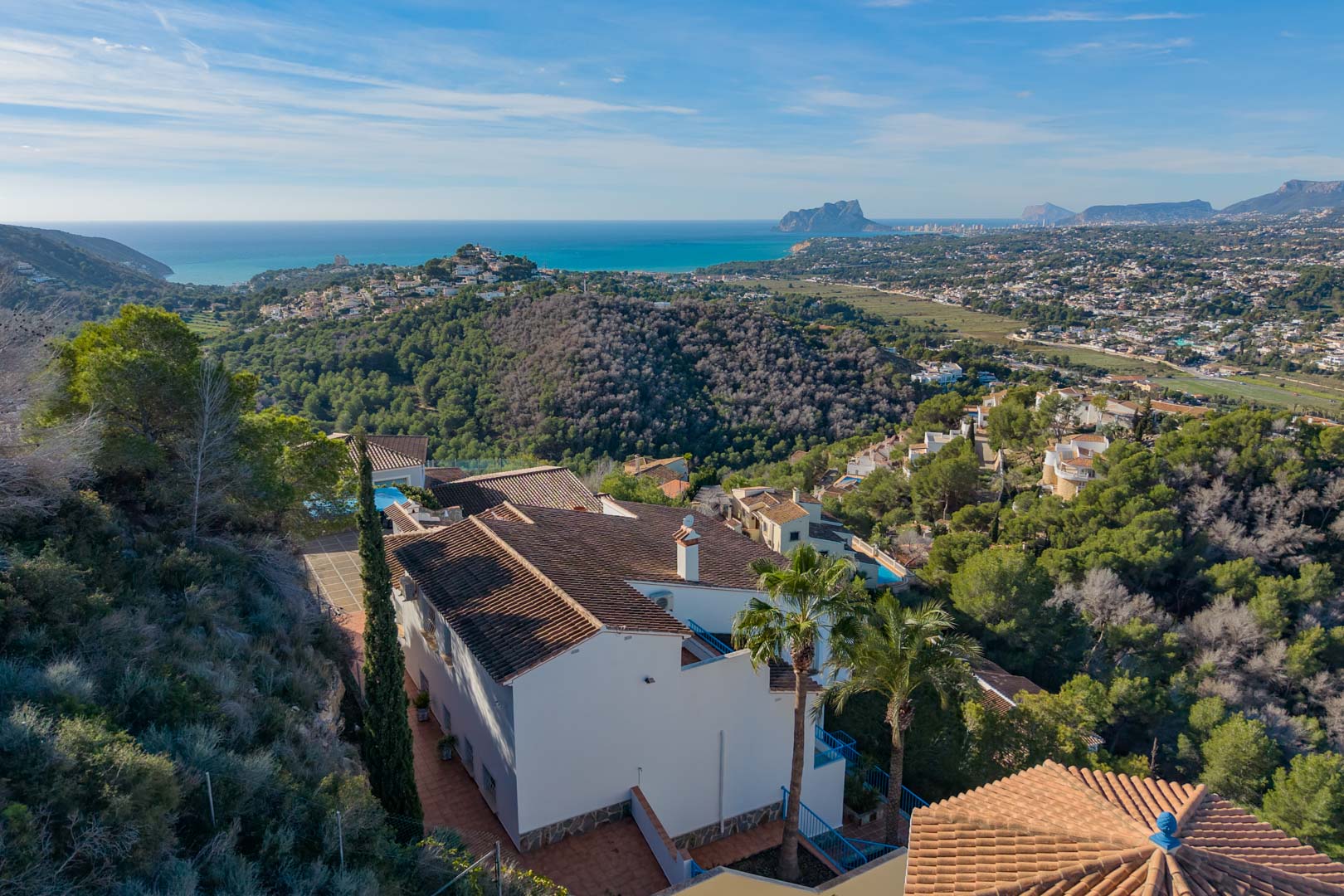 Vue aérienne de la villa à l'architecture méditerranéenne, entourée de forêts de pins avec un panorama sur la mer et le rocher d'Ifach à l'horizon.