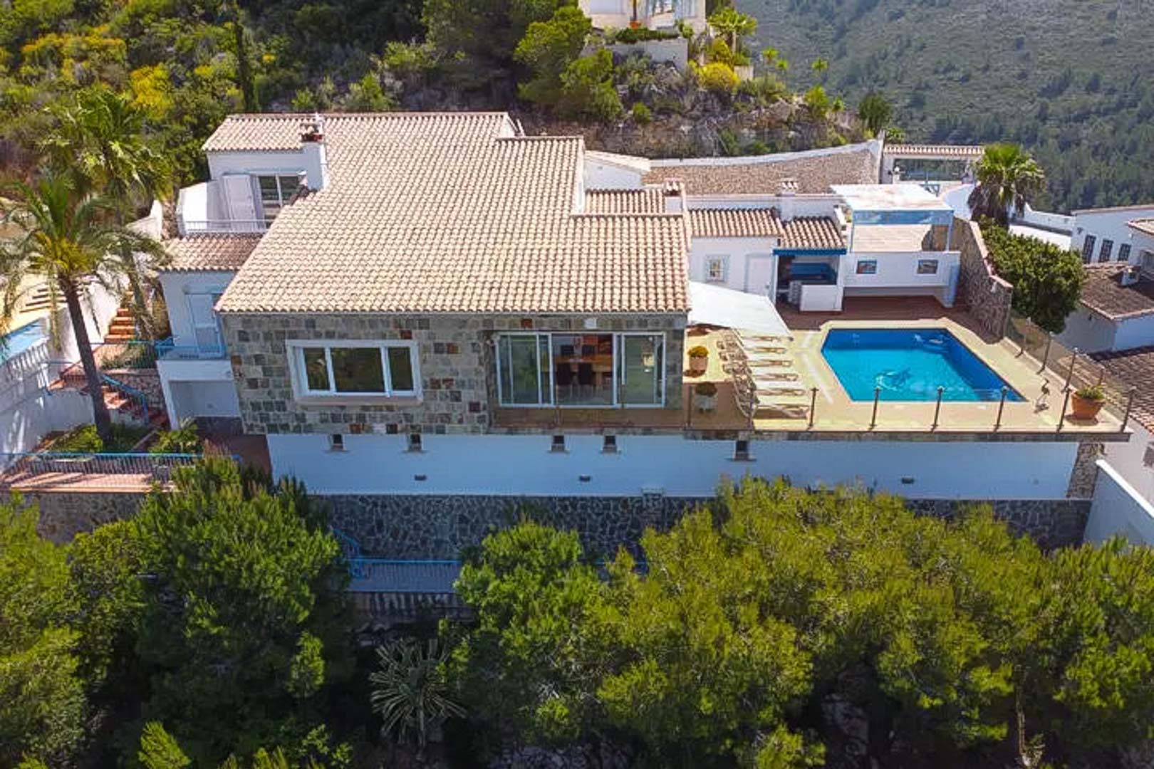 Vue aérienne de la villa avec façade en pierre naturelle, toits en tuiles et terrasse surélevée comprenant une piscine privée et un solarium.