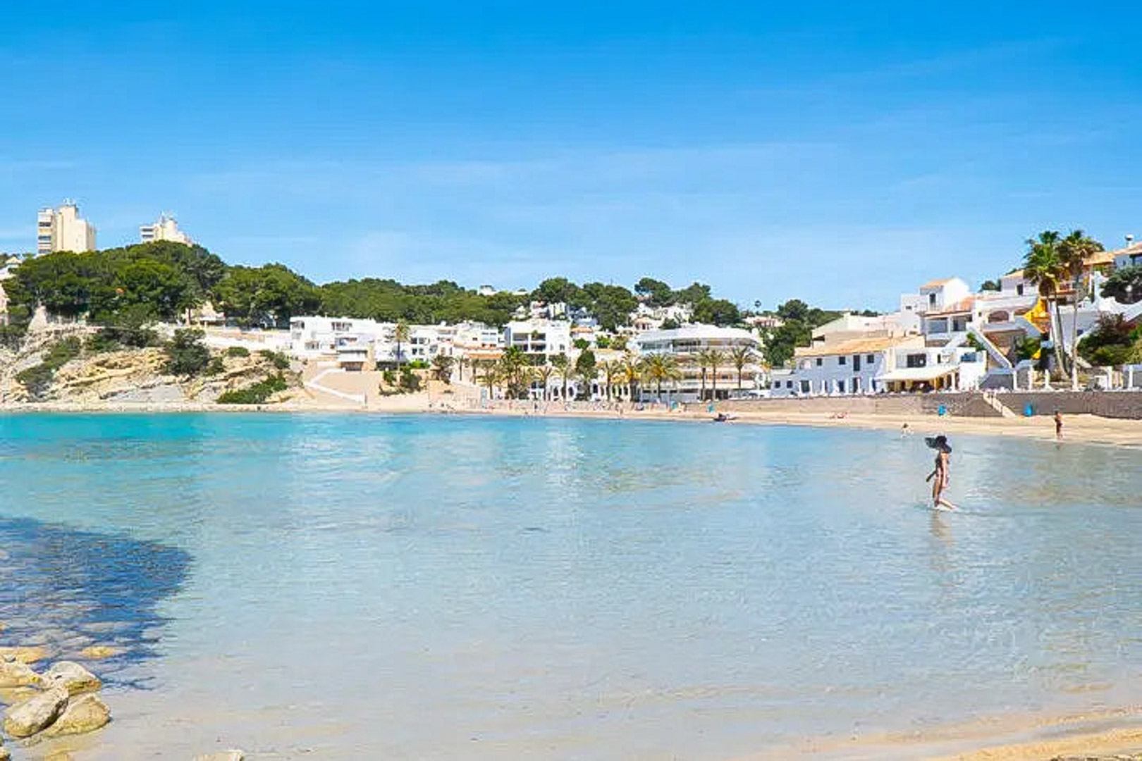 Vue panoramique de la plage d'El Portet à Moraira, avec ses eaux turquoise peu profondes et ses bâtiments blancs typiques bordant la baie.