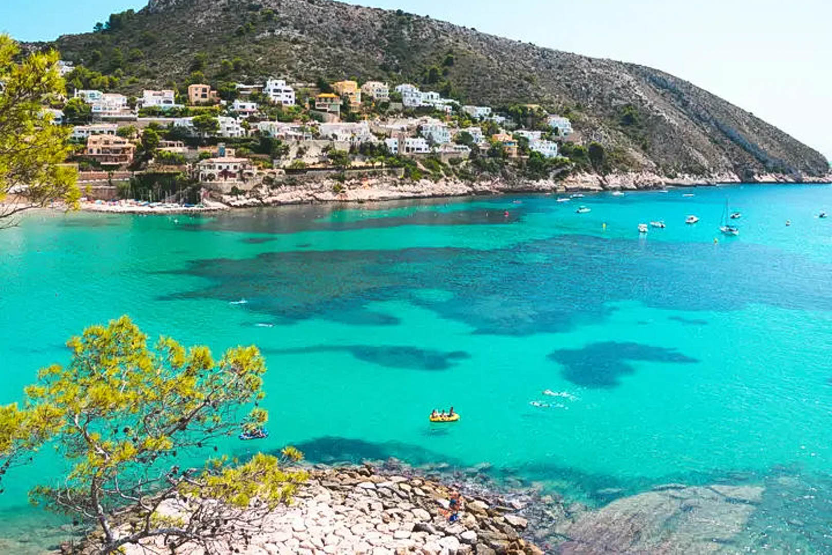 Vue panoramique d'une crique à Moraira aux eaux turquoise, bordée de pins et de villas blanches nichées sur la colline face à la mer Méditerranée.