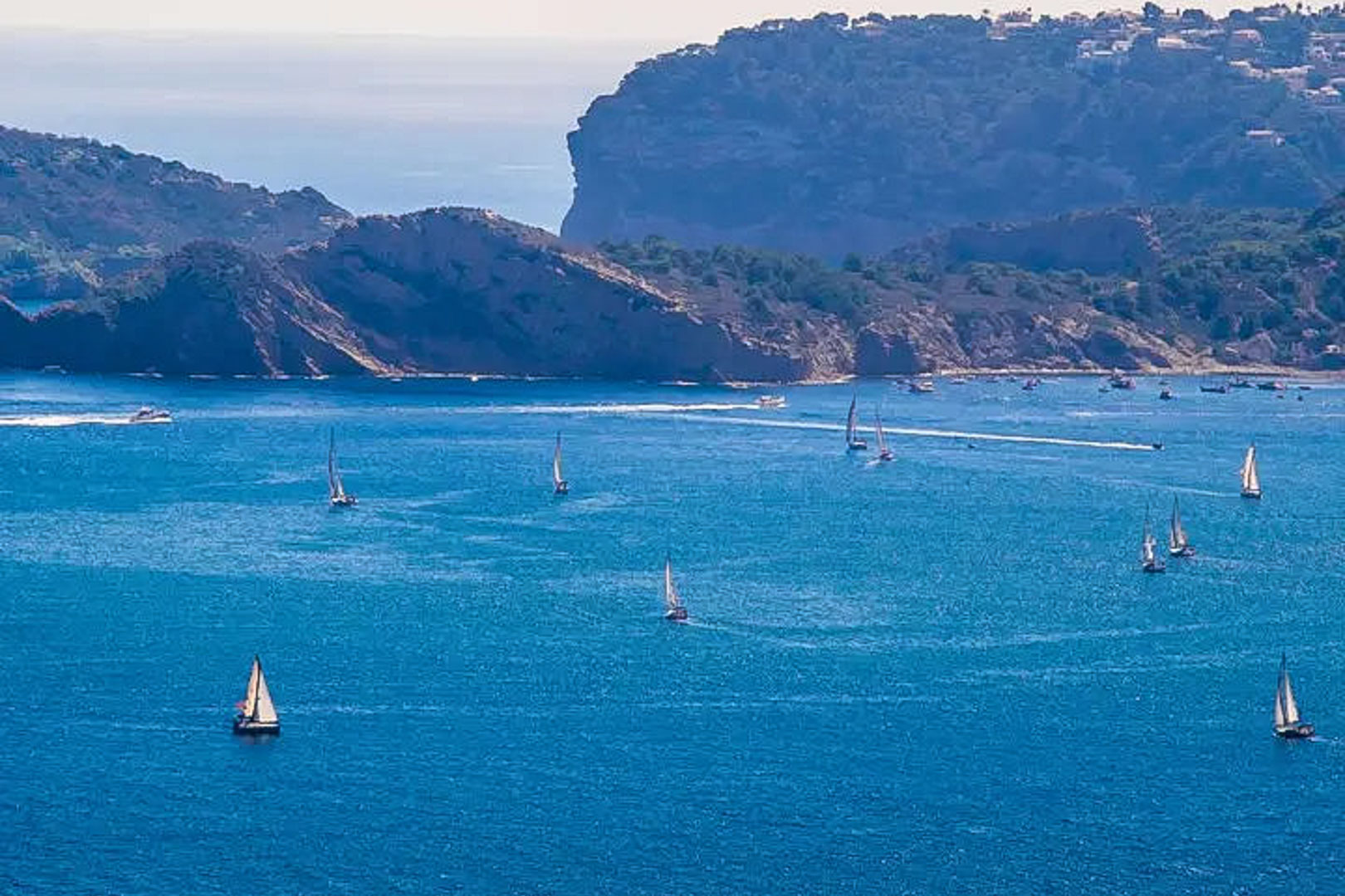 Vue panoramique sur la mer Méditerranée à Moraira, illustrant des voiliers naviguant le long des falaises escarpées de la Costa Blanca.