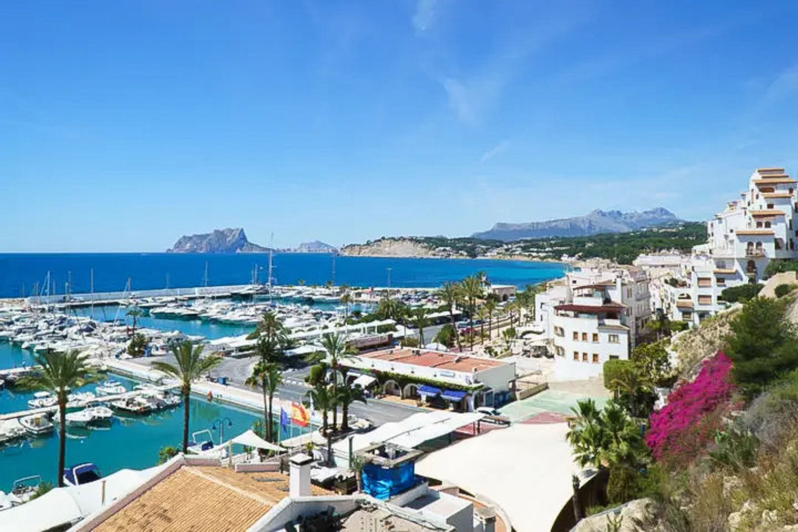 Vue panoramique sur le port de plaisance de Moraira avec le Peñón de Ifach à l'horizon, l'architecture blanche typique et les eaux turquoise de la Méditerranée.