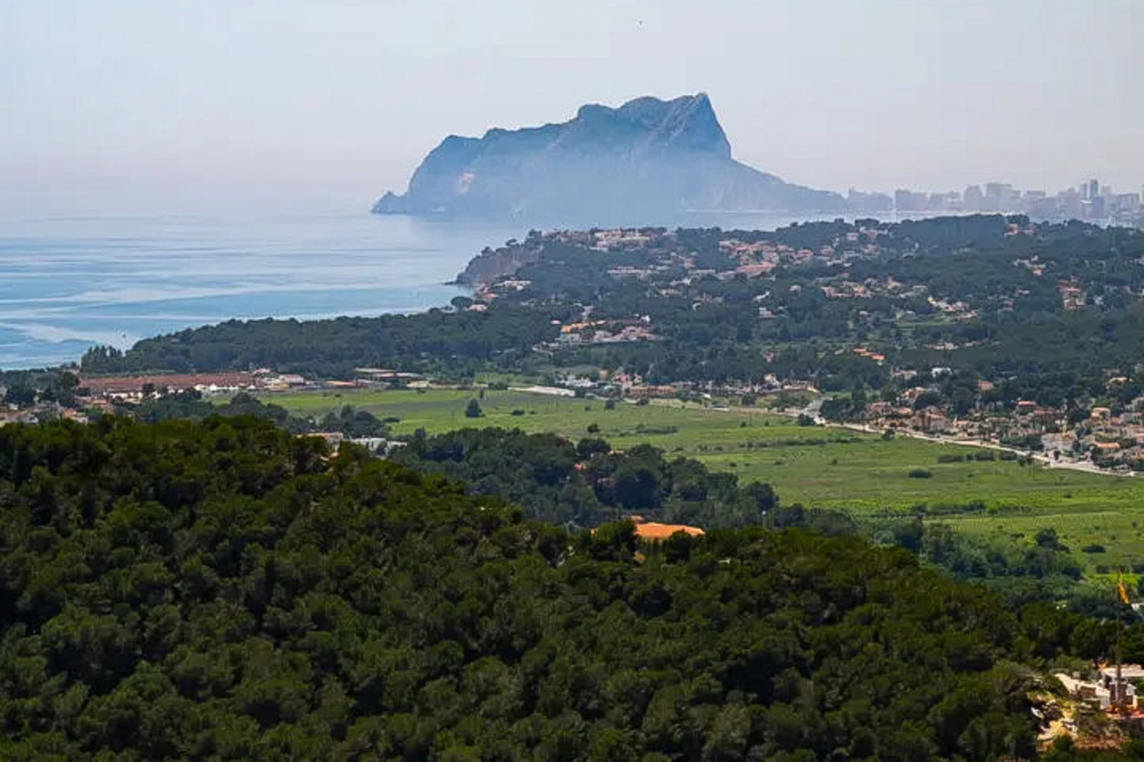 Vues panoramiques vers le Peñón de Ifach et le littoral, soulignant le contraste entre les denses forêts de pins et le bleu de la mer Méditerranée.