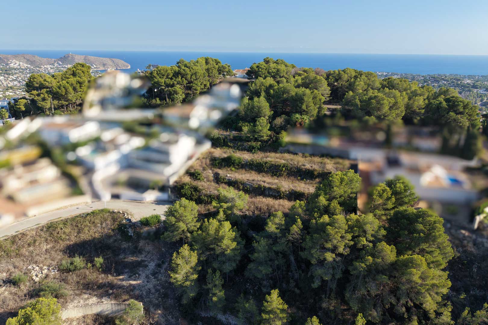 Vue aérienne du terrain urbain en terrasses, entouré de pins méditerranéens denses avec vue dégagée sur la mer et le littoral de Moraira.