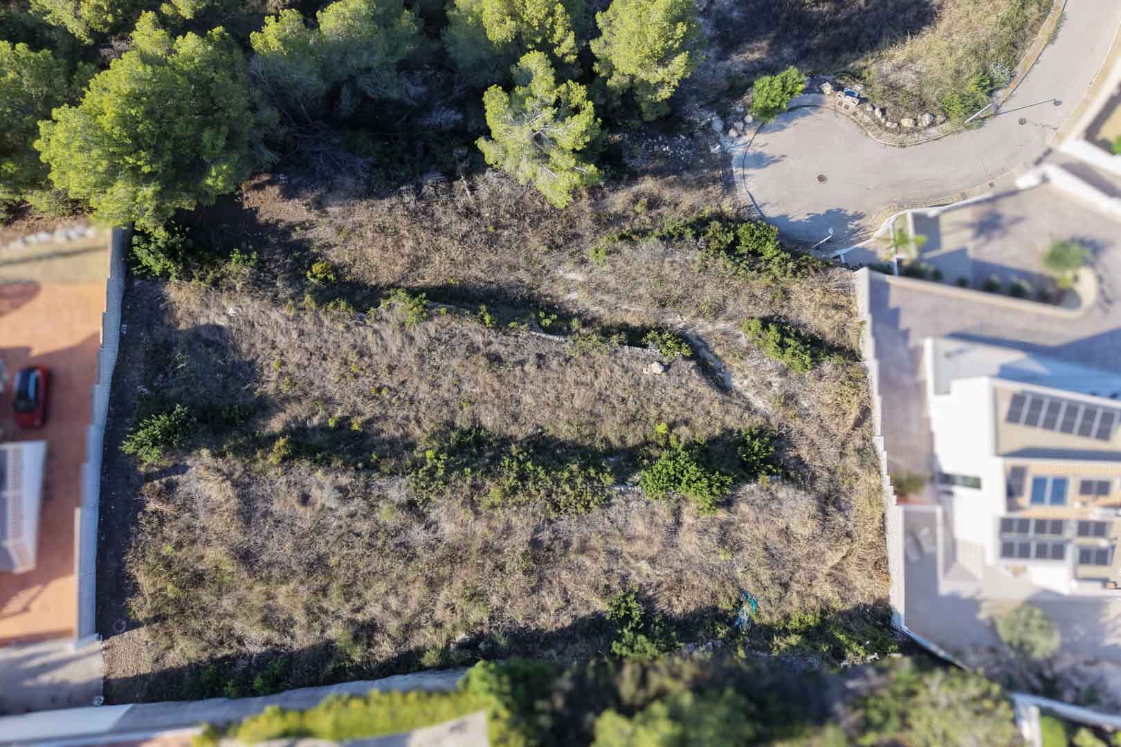 Vue aérienne zénithale du terrain urbain en terrasses avec murets en pierre, bordé de pins et situé à l'extrémité d'une impasse résidentielle calme.