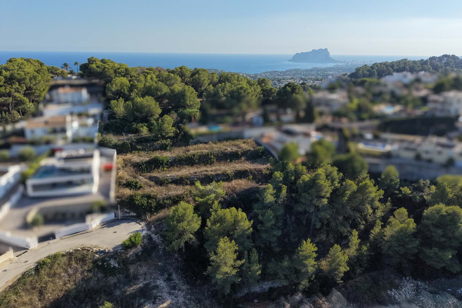 Terrain urbain en restanques avec murets de pierre et pins, offrant une vue panoramique sur la mer et le Peñón de Ifach à l'horizon.