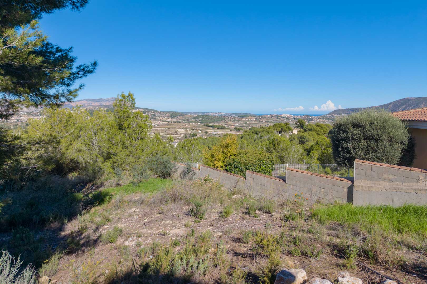 Terrain en pente offrant une vue panoramique sur la vallée et la mer. La parcelle dispose de végétation naturelle et d'un mur de clôture maçonné.
