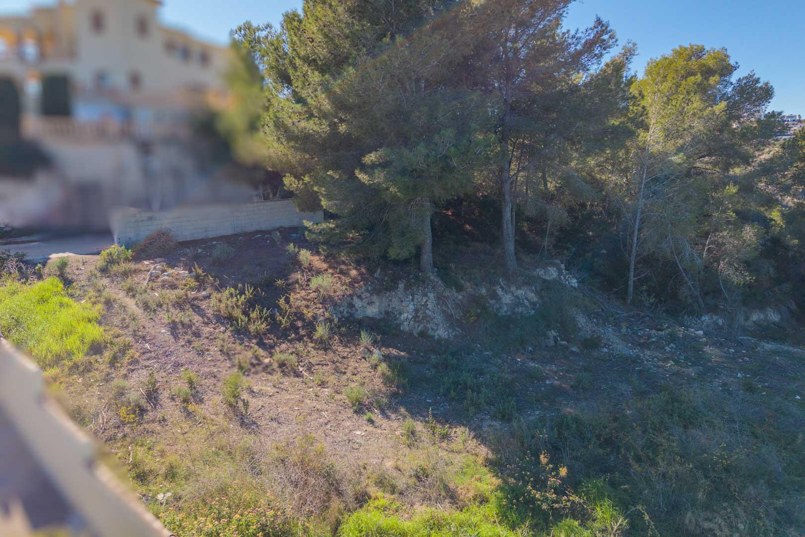 Terrain urbain en pente avec végétation méditerranéenne naturelle et pins matures, situé dans un quartier résidentiel calme de Moraira.