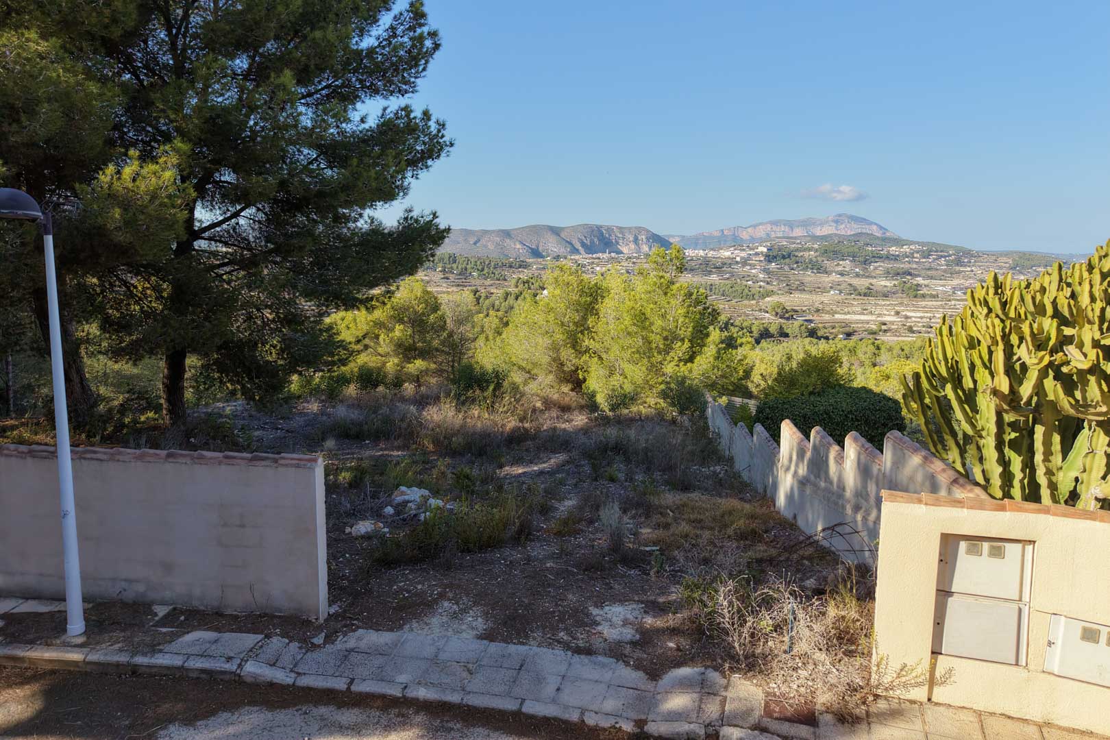 Terrain urbain surélevé à Benimeit offrant une vue dégagée sur la vallée et les montagnes. Comprend des murs de clôture, une végétation méditerranéenne et un accès par rue pavée.