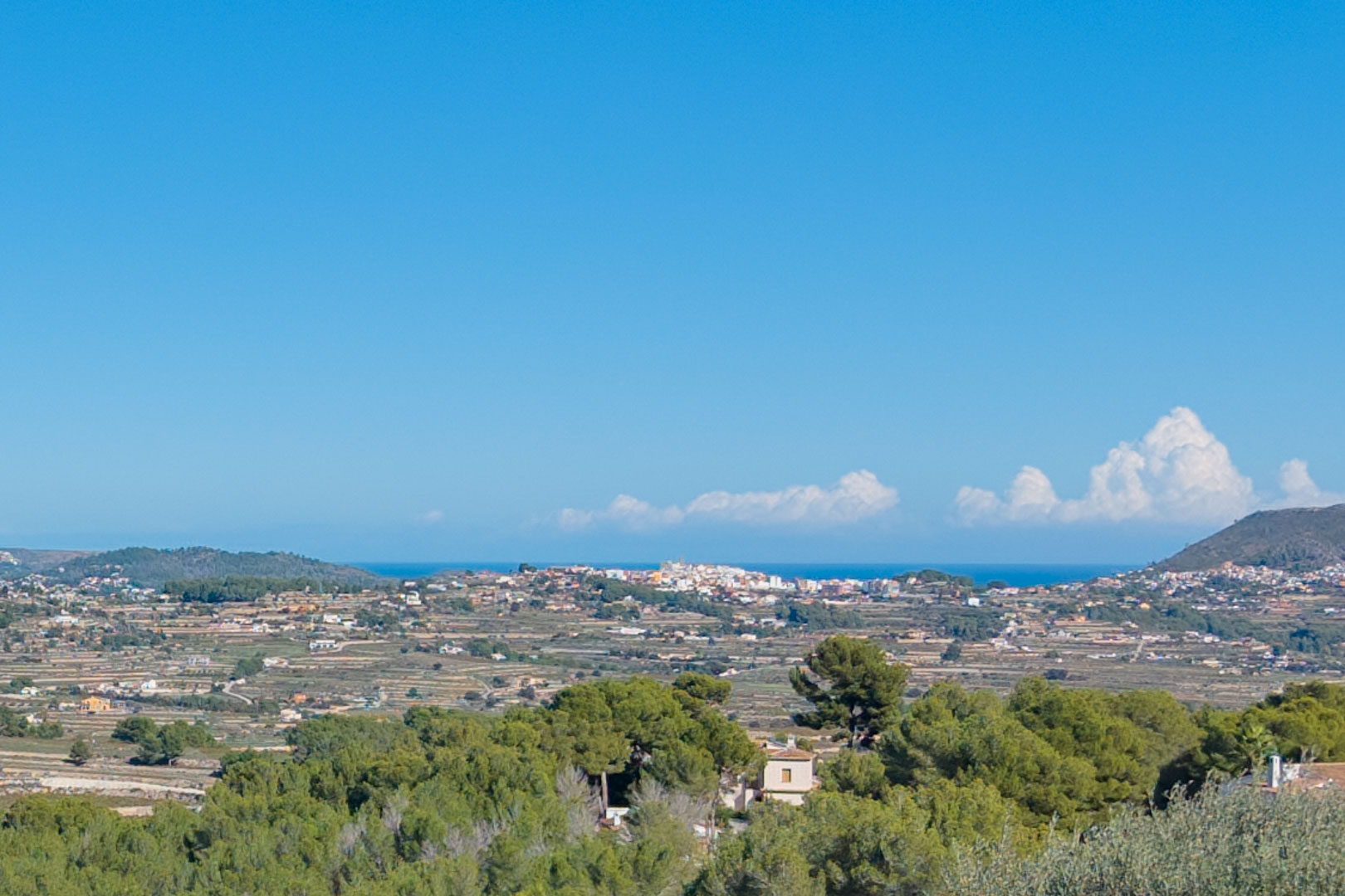 Vue panoramique depuis le terrain à Benimeit, illustrant les collines en terrasses, la végétation méditerranéenne et l'horizon marin au loin.
