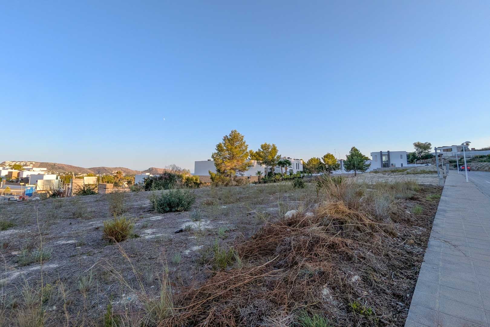 Terrain urbain plat à El Tesoro, Moraira, offrant des vues dégagées sur la vallée. Parcelle située à côté de villas contemporaines avec accès par trottoir pavé.