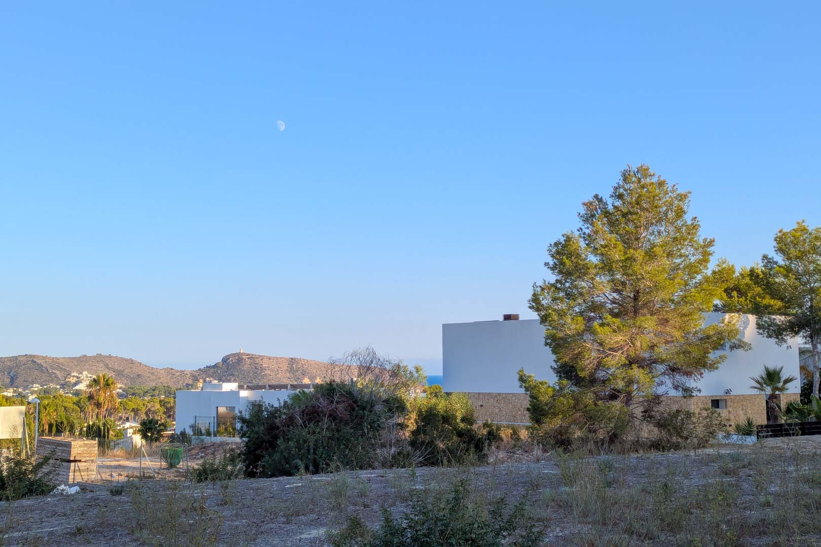 Vue depuis le terrain sur des villas contemporaines et des pins, offrant un panorama sur les collines et un aperçu de la mer Méditerranée.