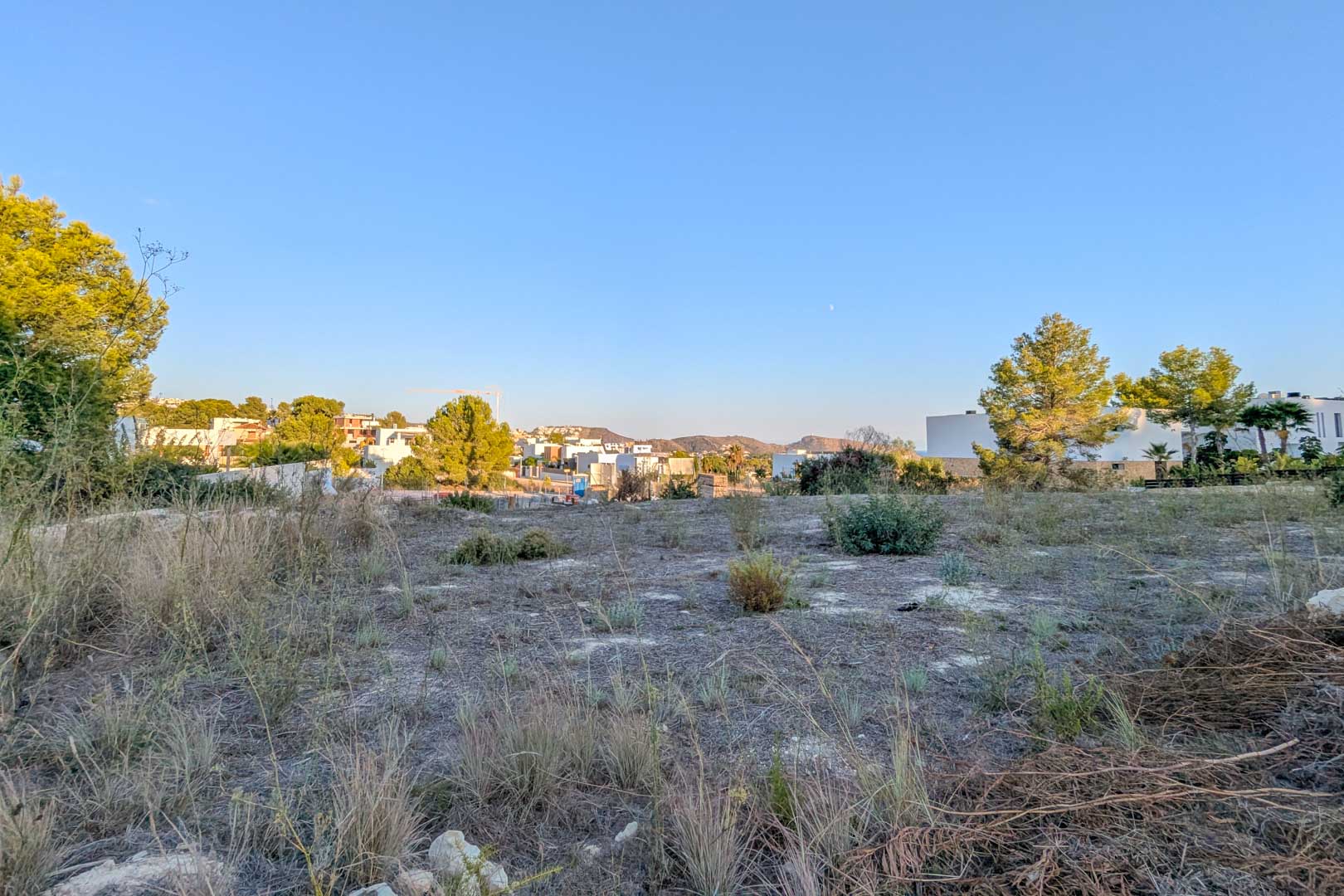 Vue panoramique du terrain plat à El Tesoro, entouré de végétation méditerranéenne avec des villas modernes et des collines en arrière-plan.