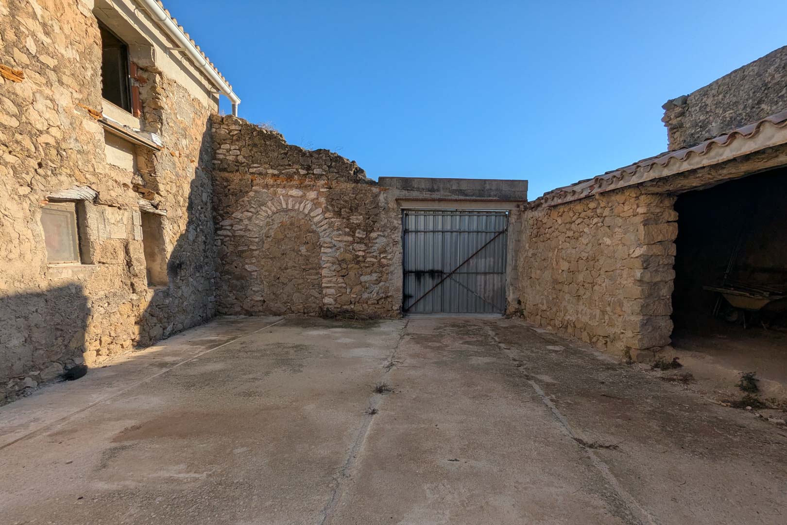 Cour extérieure avec murs en pierre, arche d'origine murée et accès aux anciennes écuries, témoignant du passé agricole.