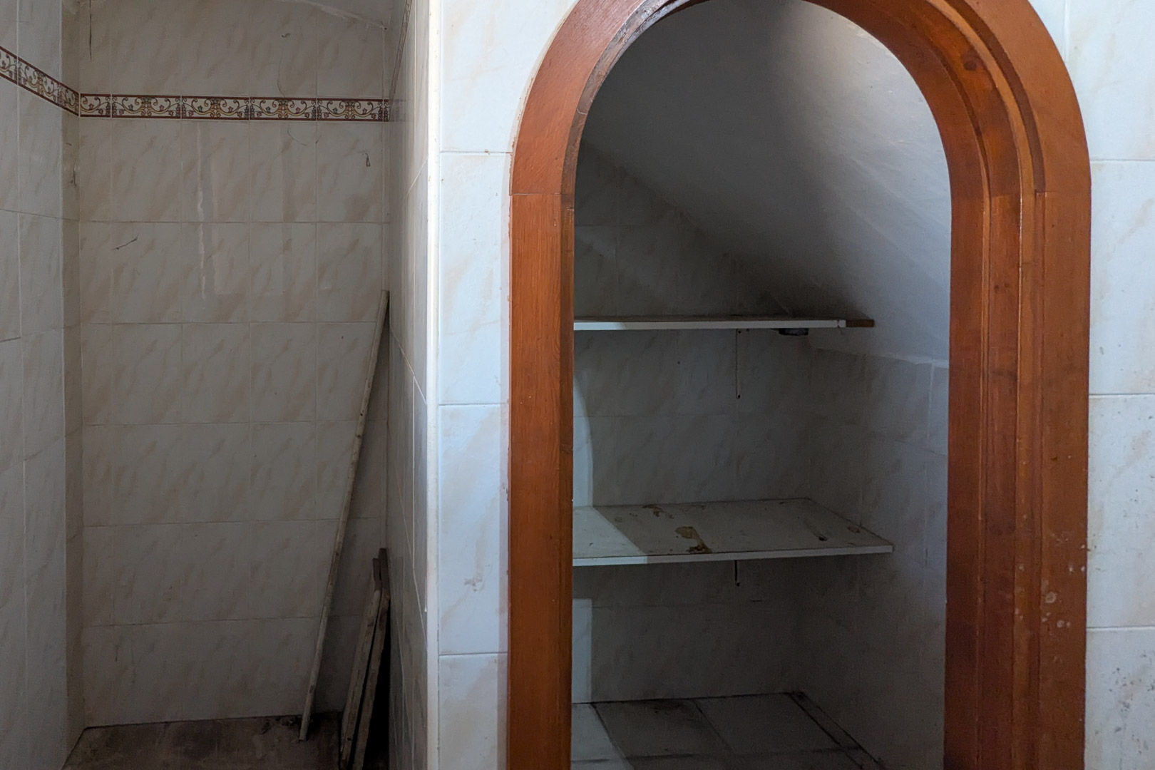 Espace de rangement sous l'escalier avec arche en bois, murs carrelés blancs et étagères, offrant un potentiel d'organisation.
