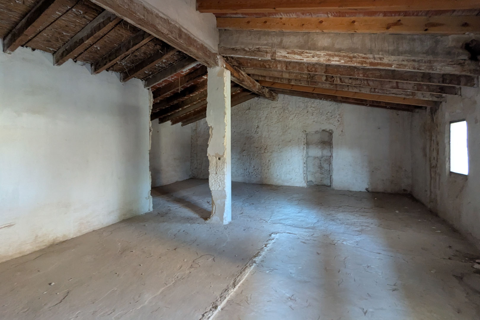 Étage supérieur ouvert révélant la charpente originale en bois d'amandier, des plafonds en canne et des murs à la chaux avec fenêtre latérale.