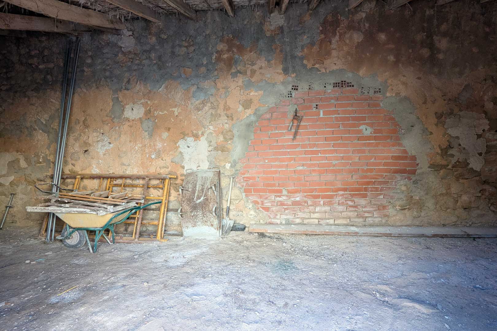 Intérieur rustique avec murs en pierre d'origine, section en briques et plafond traditionnel en poutres de bois et canisses. L'espace sert actuellement de zone de stockage.