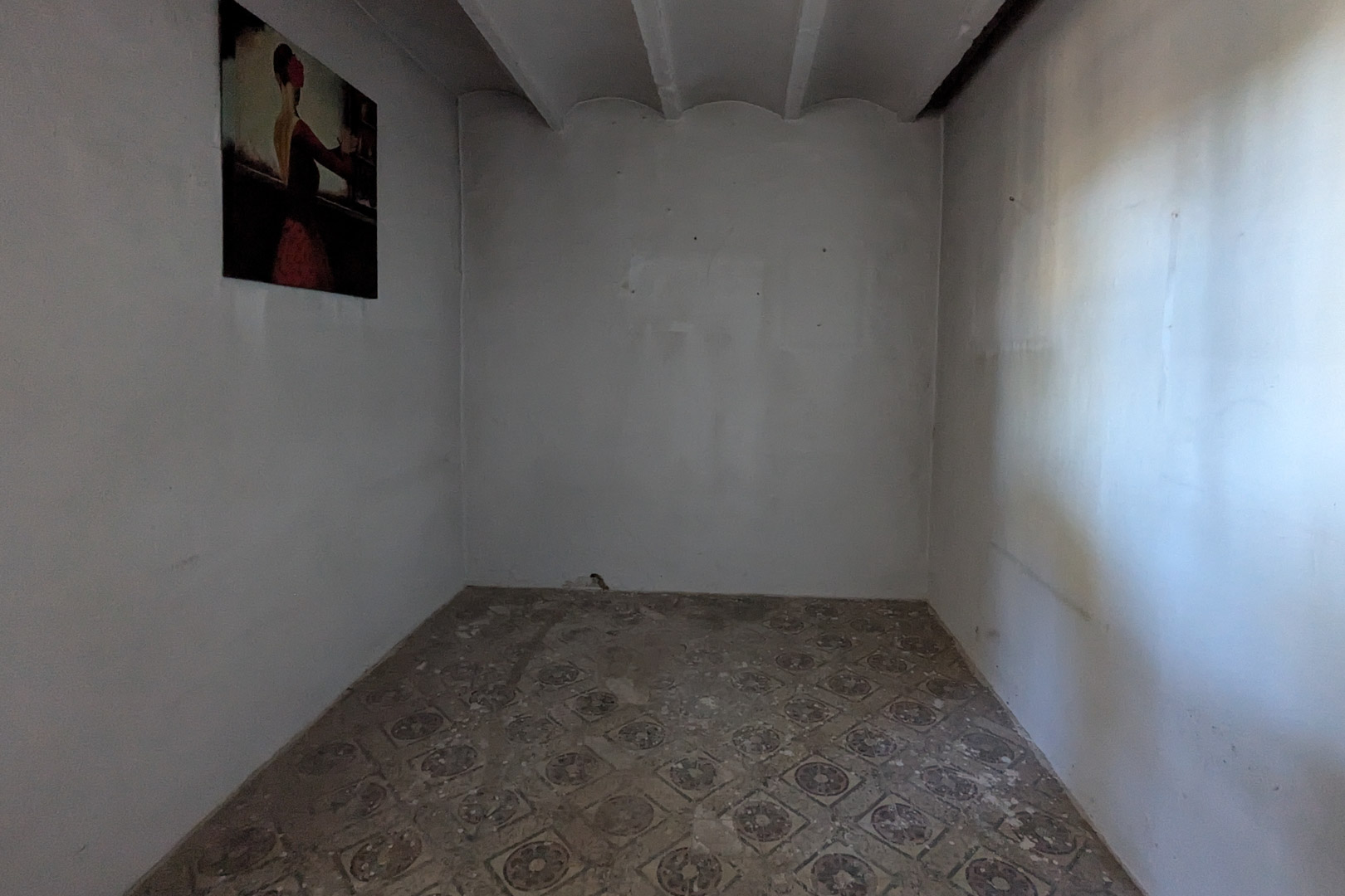 Pièce intérieure avec sol en carreaux de ciment traditionnels et plafond à poutres apparentes. Les murs blancs et la lumière naturelle soulignent le caractère rustique du lieu.