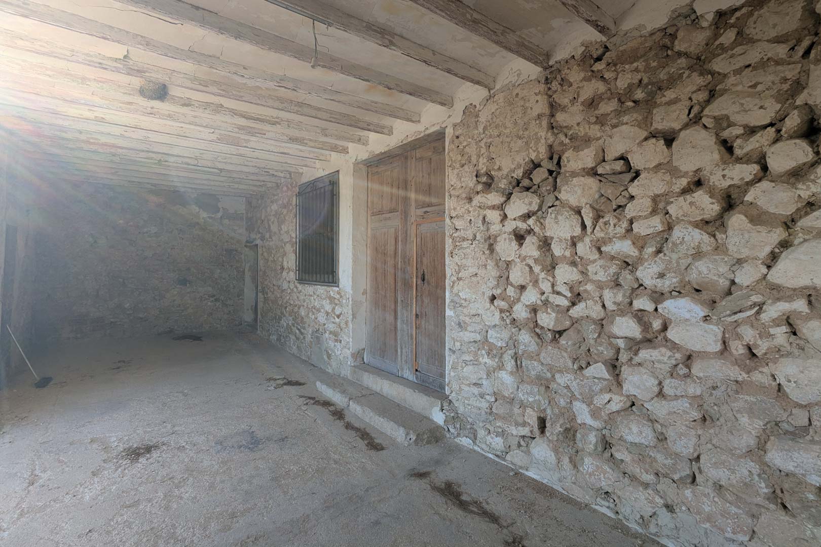 Porche couvert avec murs en pierre naturelle apparente, poutres en bois d'origine et une ancienne double porte d'entrée en bois de style méditerranéen.