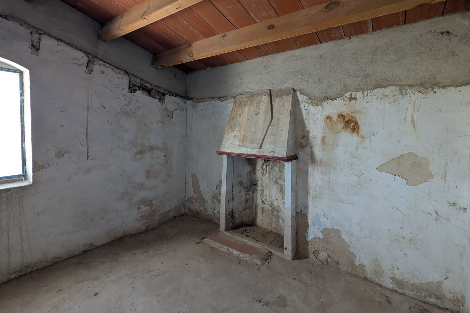 Salon rustique avec cheminée traditionnelle à hotte, poutres en bois apparentes au plafond et murs à la chaux révélant la structure d'origine.