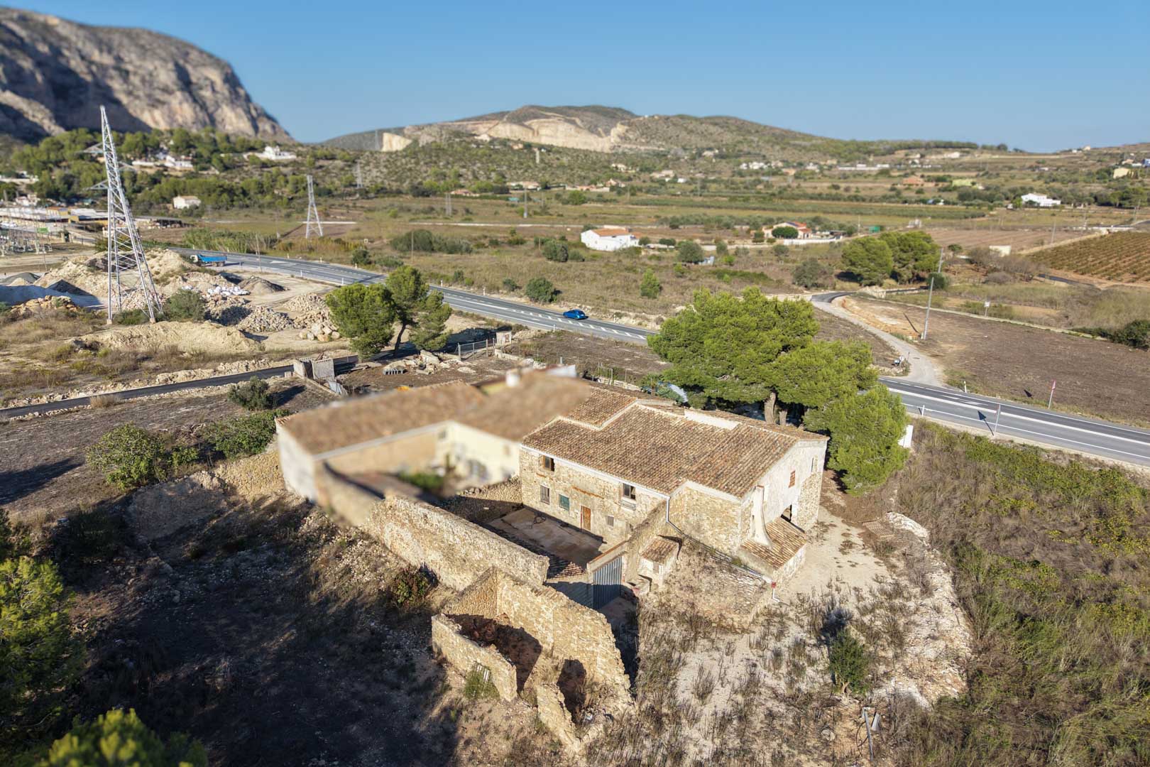 Vue aérienne de la ferme traditionnelle en pierre avec son toit en tuiles, sa cour intérieure et son vaste terrain plat entouré de montagnes à Teulada.