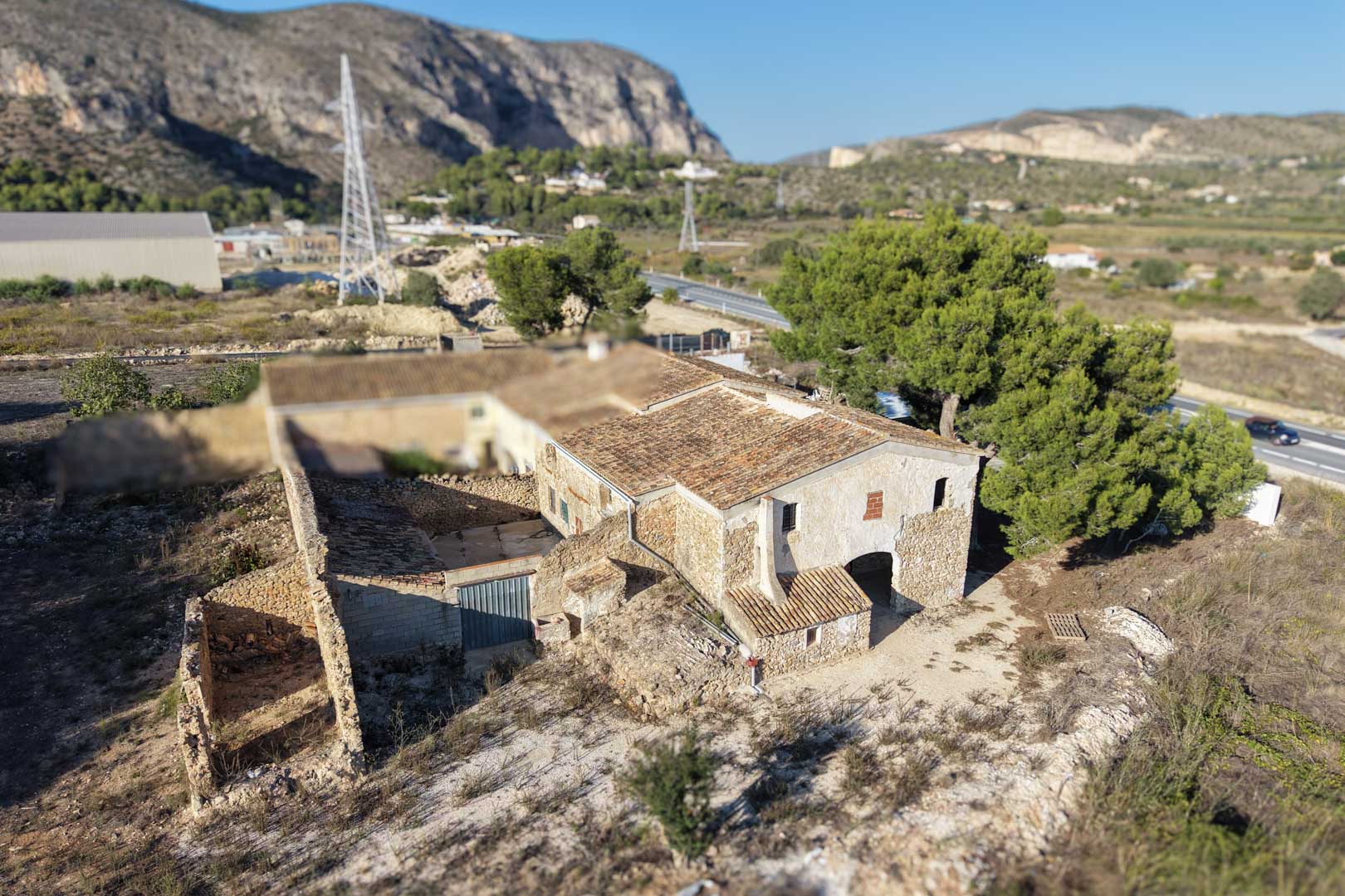 Vue aérienne de la ferme traditionnelle en pierre avec toitures en tuiles et dépendances, nichée dans un paysage rural au pied des montagnes.