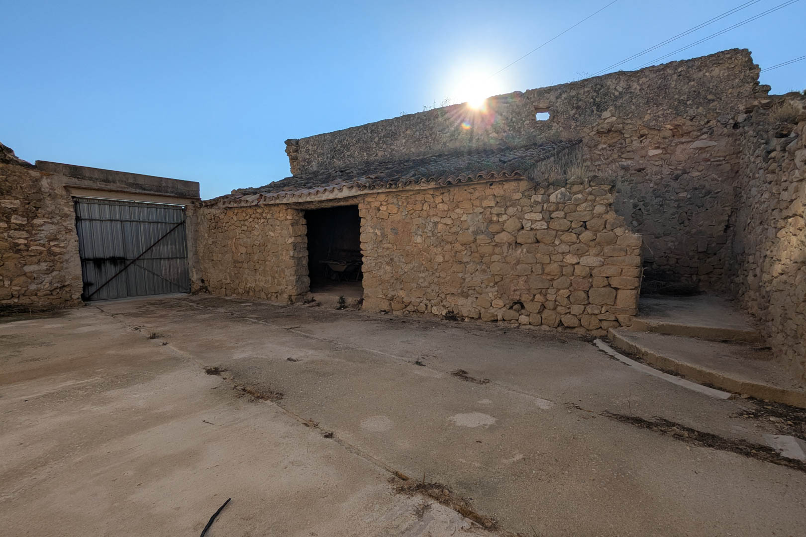 Vue extérieure des anciennes écuries en pierre naturelle, avec des murs en maçonnerie traditionnelle et une vaste cour en béton attenante.
