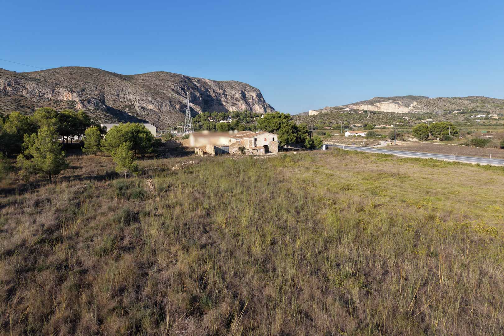 Vue panoramique de la maison traditionnelle en pierre sur un vaste terrain rural, entourée de végétation méditerranéenne et de montagnes à Teulada.