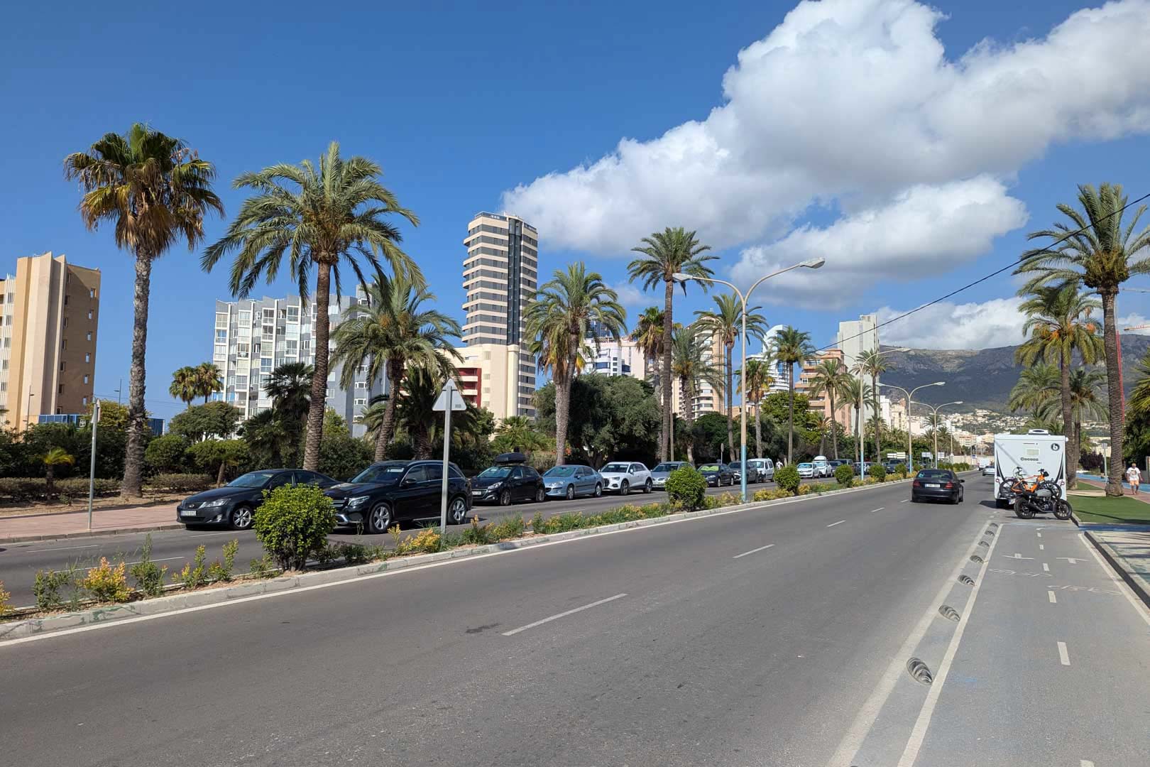 Avenue côtière avec piste cyclable, palmiers et immeubles résidentiels de grande hauteur avec les montagnes en arrière-plan.