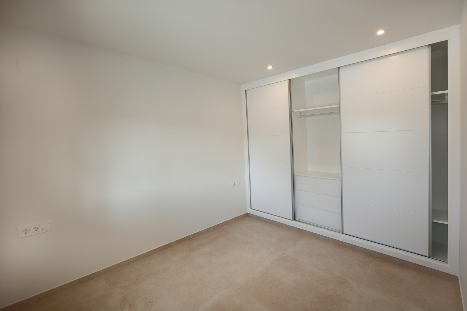 Chambre avec placard intégré à portes coulissantes laquées blanches, sol en grès cérame et éclairage LED encastré au plafond.