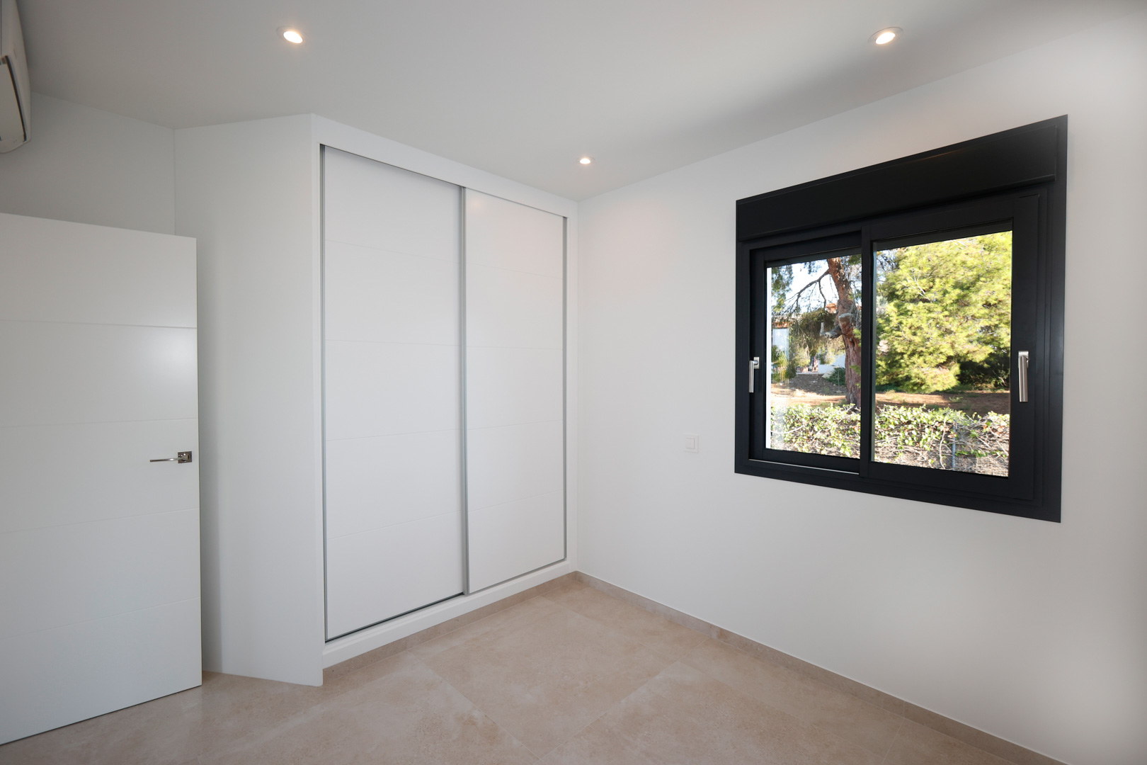 Chambre moderne avec placard intégré à portes coulissantes blanches, sol en grès cérame et fenêtre en aluminium noir avec vue sur le jardin.