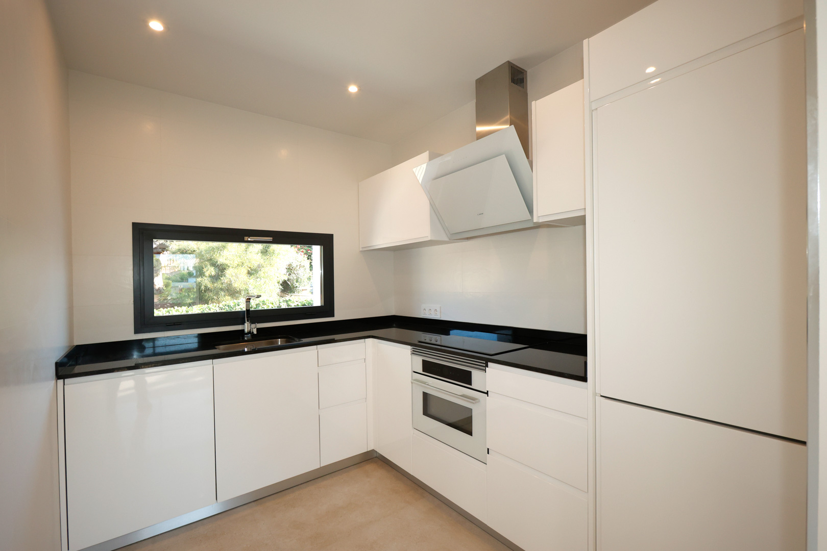 Cuisine moderne avec meubles blancs, plan de travail en Silestone noir, électroménagers Bosch intégrés et fenêtre offrant une vue sur le jardin.