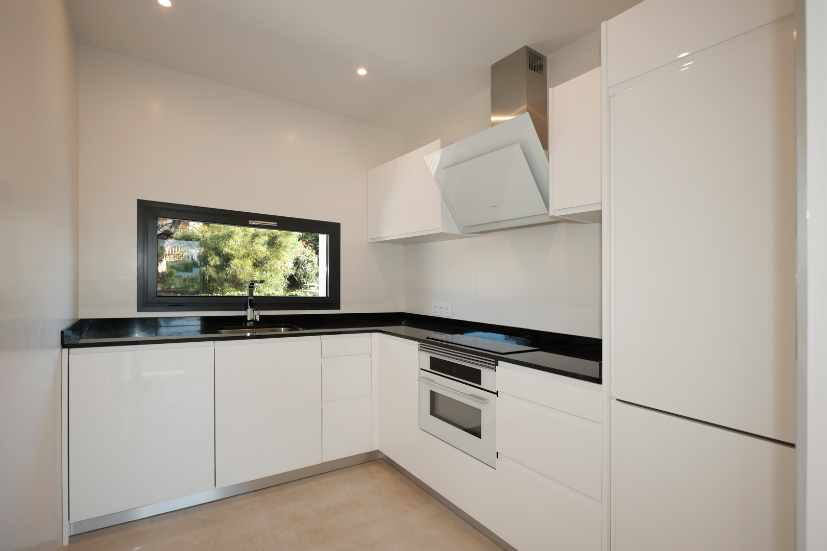 Cuisine moderne avec placards laqués blancs, plan de travail en Silestone noir, électroménager Bosch intégré et fenêtre sur le jardin.